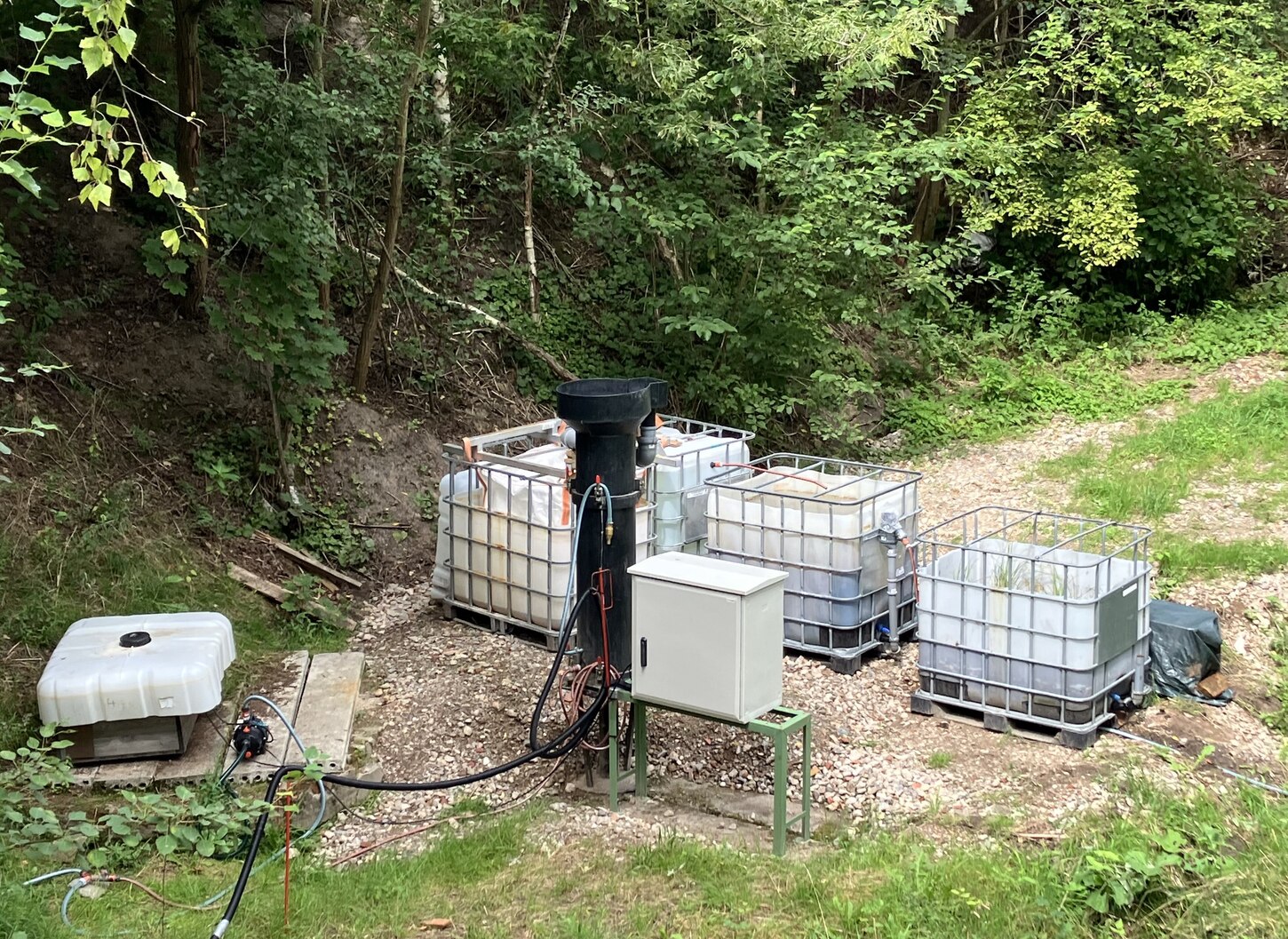 Zu sehen sind in Reihe geschaltete Container zur Wasserreinigung auf einer Wiese.